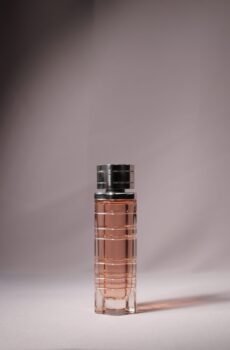 Sleek glass perfume bottle with pink liquid displayed against a neutral backdrop.