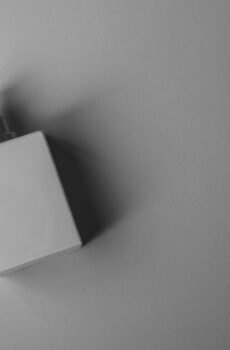 A sleek white perfume bottle photographed on a gray background with soft, muted lighting.